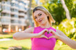 Young pretty blonde woman at outdoors With glasses making heart with hands