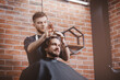 Barber shop, warm toning photo. Man in barbershop chair, hairdresser styling his long hair