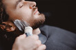 Barber applies shaving foam with brush to man beard in barbershop, warm toning, top view.
