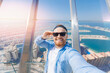 Young man tourist make selfie photo on background skyscrapers in Dubai on view point. UAE business tourism for cryptocurrency concept