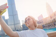 Tourist young woman make selfie photo on phone on background skyscrapers of Dubai UAE with sunlight