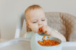 Portrait of happy young baby boy In high chair eating pasta