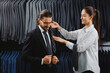 Young beautiful female consultant offering accessory tie to handsome businessman in menswear store. Boutique shop of classic clothes for business men