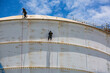 © chitsanupong - Male two worker down height tank roof rope access safety inspection thickness weld of storage tank.