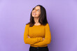 © luismolinero - Young mixed race woman isolated on purple background looking up while smiling