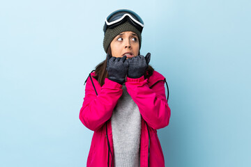 Wall Mural - Mixed race skier girl with snowboarding glasses over isolated blue background nervous and scared putting hands to mouth.