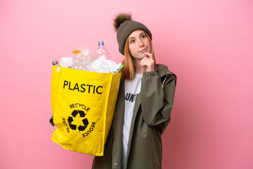 Wall Mural - Young redhead woman holding a bag full of plastic bottles to recycle isolated on pink background and looking up