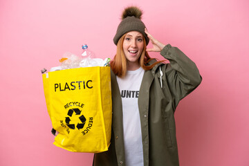 Wall Mural - Young redhead woman holding a bag full of plastic bottles to recycle isolated on pink background with surprise expression