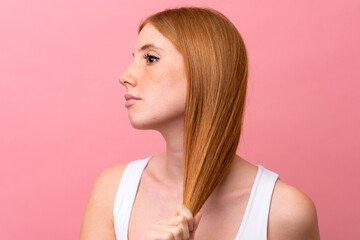 Wall Mural - Young redhead woman isolated on pink background touching her hair. Close up portrait