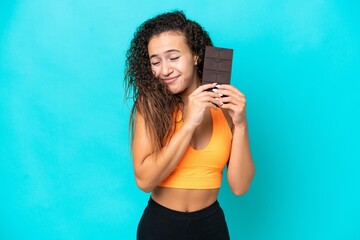 Wall Mural - Young Arab woman isolated on blue background taking a chocolate tablet and happy