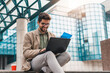 © Dorde - Handsome business man working on laptop while sitting outside a modern business building in downtown financial district.