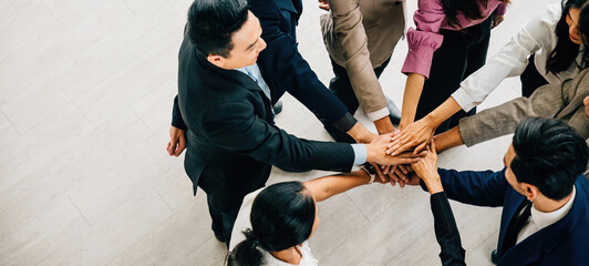 Wall Mural - A top perspective reveals four diverse businesspeople standing in a circle stacking their hands. This image conveys the concepts of unity teamwork and global collaboration.