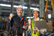 Senior male engineer and Asian female engineer raising hands to work success. Teamwork with a laptop, smile in industrial factory.