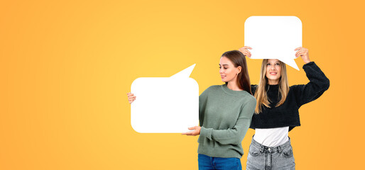 Smiling women holding mockup speech bubbles on empty orange background