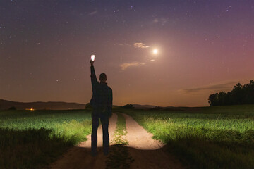 Wall Mural - man silhouette shining with mobile phone on way between field under night sky with star and moon