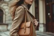 © anatolir - Stylish young woman in a chic jacket carries a luxury handbag along an urban sidewalk