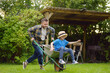 Wheelbarrow pushing by dad in domestic garden on warm sunny day. Active outdoors games for family with kids in the backyard