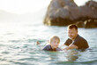 Happy child and mature father have fun swimming in sea or lake at sunset. Dad teaches his little son to swim. Active holidays for families with kids during the summer vacation at resort