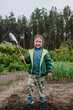 Little boy, happy child helps to dig soil with a shovel in the garden outdoors. Photography, portrait, agricultural concept, childhood.