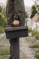 Wall Mural - A man, a professional worker, a repairman holds a suitcase, a briefcase with tools in his hands while providing services in the workshop. Close-up photography, construction work concept.