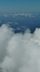 Wall Mural - Flying through beautiful white fluffy clouds in sky over blue sea. Airplane travel background. Vertical video