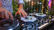 © thanakrit - DJ mixing tracks on a console at an outdoor party with colorful lights in the background