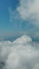 Wall Mural - Flying through beautiful white fluffy clouds in sky over blue sea. Airplane travel background. Vertical video