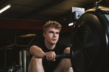 Low angle shot of a handsome male athlete looking focused, exercising on a row gym machine