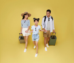 Happy fun asian family vacation portrait. Father, mother and daughters ready for travel flight with suitcase isolated on yellow studio background.