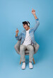 Happy young asian man listening to music with headphone dancing on chair isolated on blue background. People lifestyle concept.