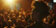 © Kishore Newton - Engaging image of a young woman speaking passionately into a microphone at a lively event, highlighted by a warm, golden backlight and an attentive audience.