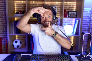 Poster - Middle age man with beard playing video games wearing headphones smiling making frame with hands and fingers with happy face. creativity and photography concept.