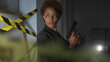 © Krakenimages.com - Focused black woman holding a gun in dimly-lit crime scene with caution tape