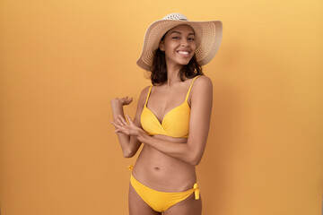 Poster - Young hispanic woman wearing bikini and summer hat inviting to enter smiling natural with open hand