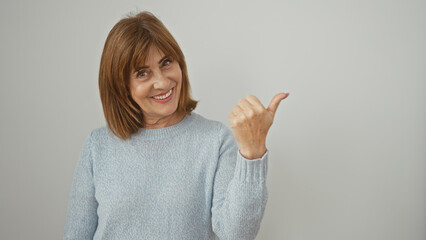 Wall Mural - A smiling middle-aged woman in a sweater gestures with her thumb against a white background