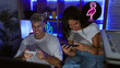 © Krakenimages.com - A smiling man and focused woman play video games together in a neon-lit gaming room at night, depicting leisure and companionship.