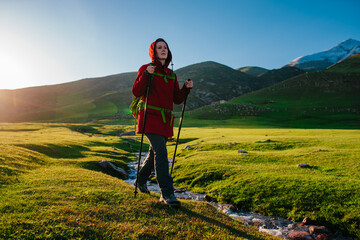 Sticker - Young woman tourist walks along stream in picturesque mountain valley on a sunny day