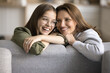 Cheerful beautiful mother and teenage daughter kid enjoying close relationships, leisure time at home, conversation, sitting on couch, smiling, laughing, leaning hands on back of comfortable furniture
