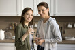 Happy mother and beautiful teenager daughter kid holding glasses, drinking natural clear water at home, standing in kitchen, looking at camera, smiling for portrait, promoting hydration balance