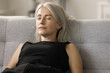 Peaceful relaxed pretty mature lady sleeping on cozy couch at home, sitting on sofa, leaning on soft back with closed eyes, breathing fresh air, reloading mind, enjoying leisure, break