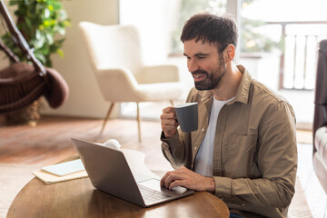 Aufkleber - A man in a casual attire is sitting at a table, focusing on his laptop screen. Beside him, there is a cup of coffee, suggesting a working environment