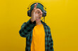 Smiling Asian man in a beanie and casual clothes gives an okay sign while listening to music or a podcast on his headphones. Isolated on a yellow background.