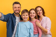 © Prostock-studio - A man is standing with his family, capturing a selfie with a smartphone. They are smiling and posing together for the self-portrait.