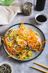 Canvas Print - Funchoza salad with fresh cucumber and Korean carrots on a plate on the table vertical view