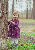 Fototapeta  - blond baby in a colored dress running in a forest glade with flowers