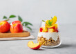 Greek yogurt parfait with peach and granola in a glass on a light background with fresh fruits. Healthy eating concept. Nutritious summer breakfast. Copy space.