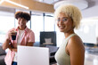 In modern office, two biracial coworkers holding coffee, laughing together