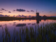 Windmill in the Netherlands. Historical buildings in the Netherlands. Reflections on the surface of water. Image for postcards, background, design. Landscape during sunset. Bright sky and clouds.