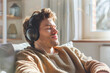 © Alexandra - Young adult male in casual sweater, eyes closed, listens to music on headphones with a content smile, bathed in warm sunlight