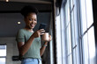 © Wavebreak Media - At office, African American businesswoman holding coffee, looking at phone, copy space